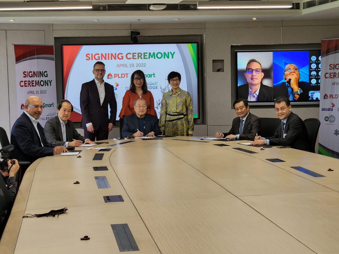 (seated, centre) PLDT Chairman Manuel V. Pangilinan leads the signing ceremonies with PLDT, Smart, edotco, EdgePoint, Axiata and DigitalBridge representatives. The other signatories are, (from left) Suresh Sidhu (CEO, EdgePoint), Justin Chang (Managing Director, Head of Asia, DigitalBridge), Mohamad Adlan Ahmad Tajudin (CEO, edotco Group), Annis Sheikh Mohamed (CFO, edotco Group).  Standing, from left: Joachim Horn (Next-Generation Solutions Advisor, Smart), Marilyn V. Aquino (Chief Legal Counsel, PLDT) and Anabelle L. Chua (CFO, PLDT). Witnessing the event on-screen are Alfredo S. Panlilio (President and CEO, PLDT and Smart) and Izzaddin Idris (President and Group CEO, Axiata).